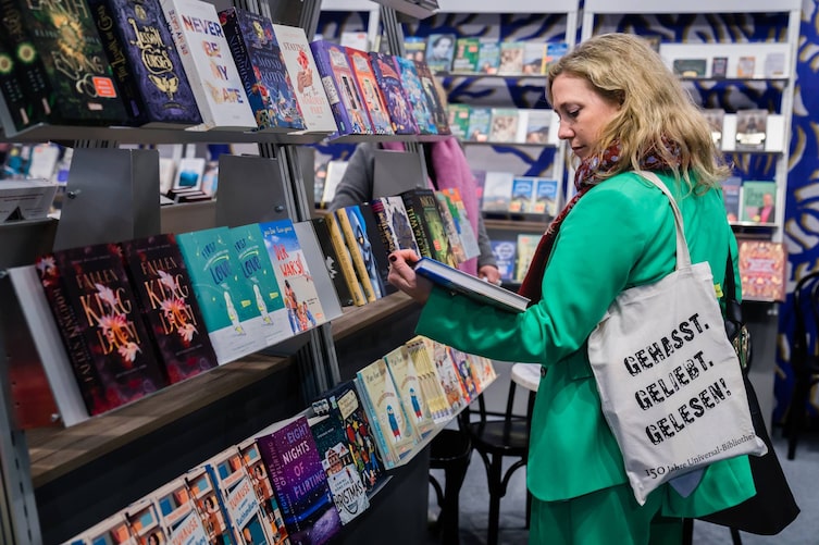 Frau steht vor einem Bücherregal und liest den Klappentext eines Buches